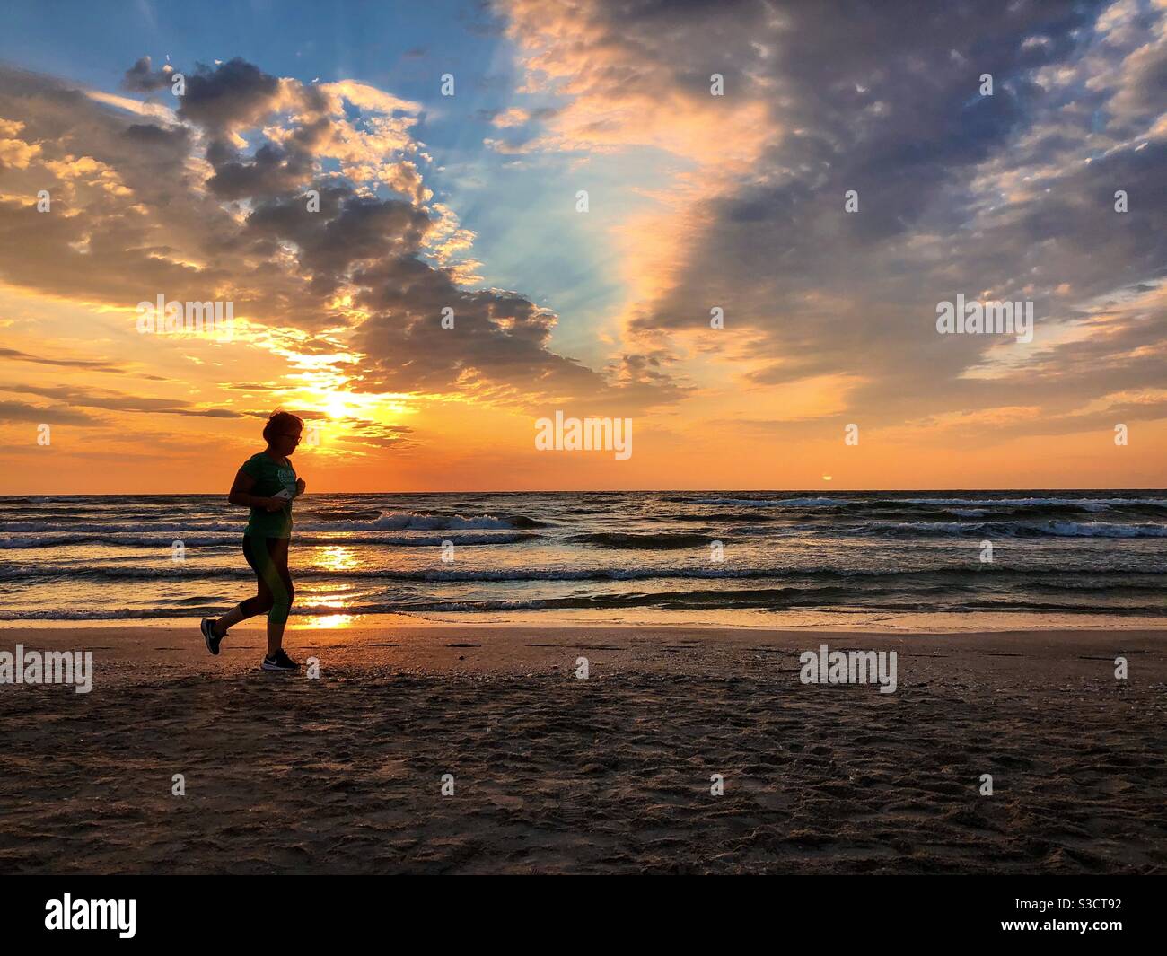 Silhouette of woman jogging on the beach at sunrise - Smartphone Captured Stock Image