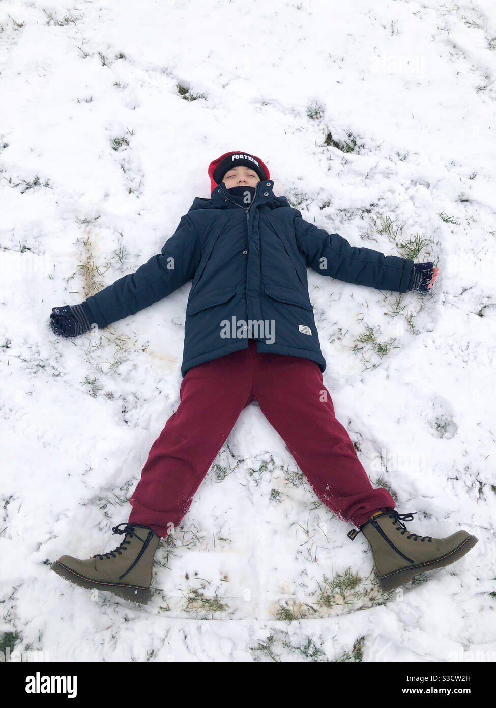 A child lying down on the floor in snow making a snow angel. - Smartphone Captured Stock Image