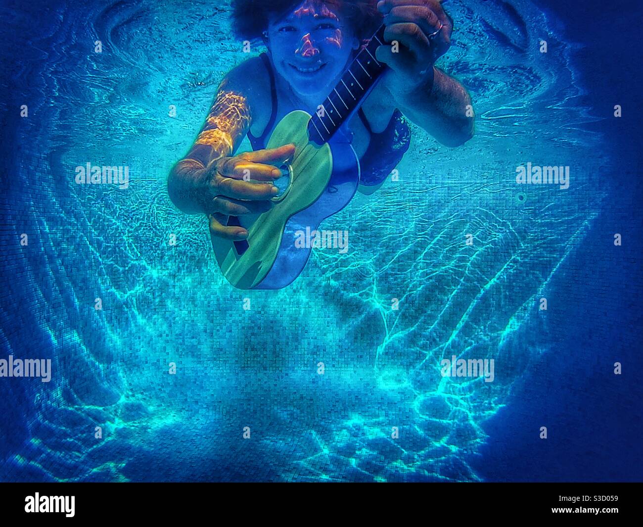 Woman playing a ukulele underwater in a swimming pool Stock Photo