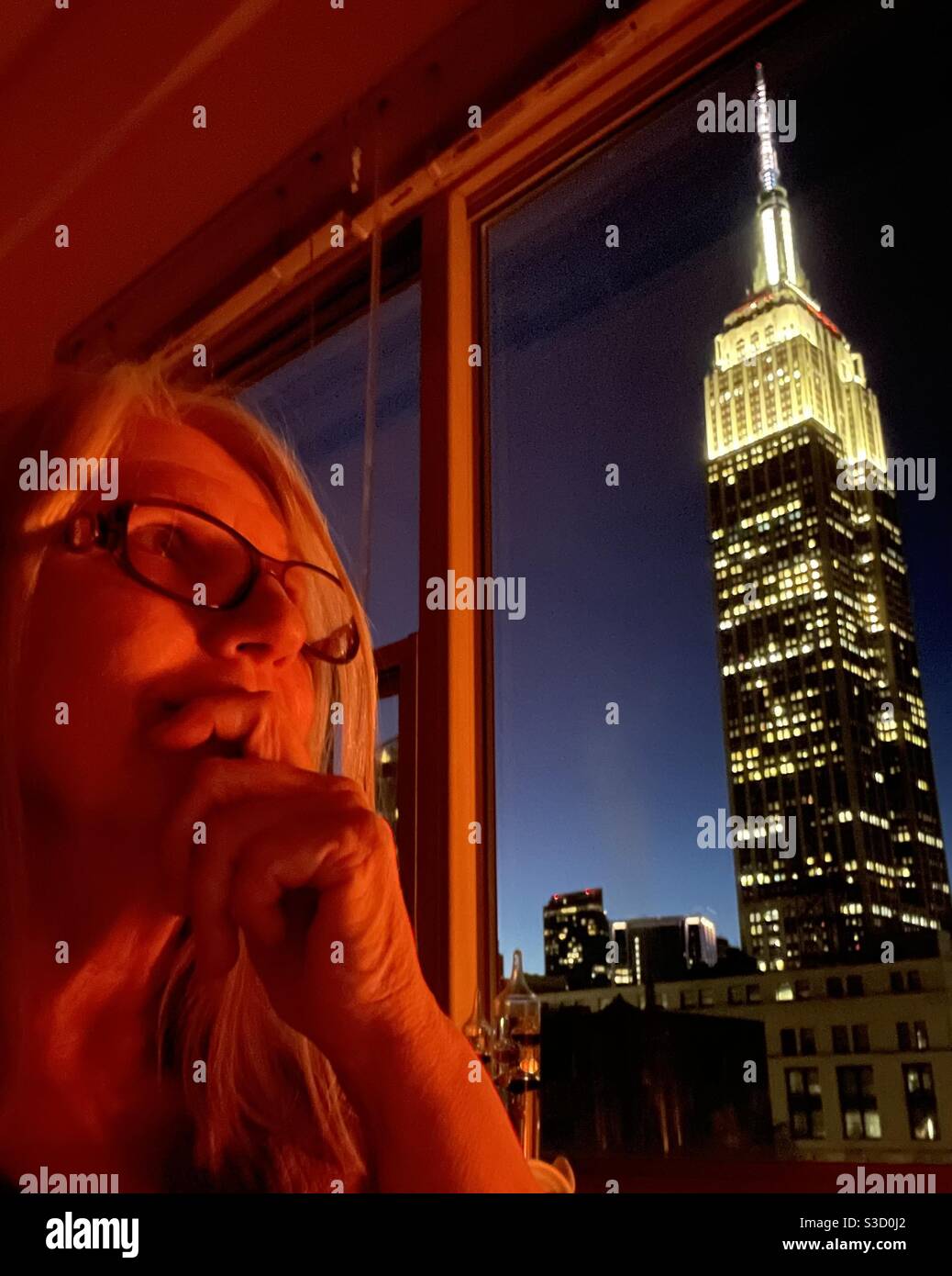 The magnificent Empire State Building, as seen from a Park Avenue apartment window, causes deep contemplation in a woman whose face is lit by warm candlelight. - Smartphone Captured Stock Image