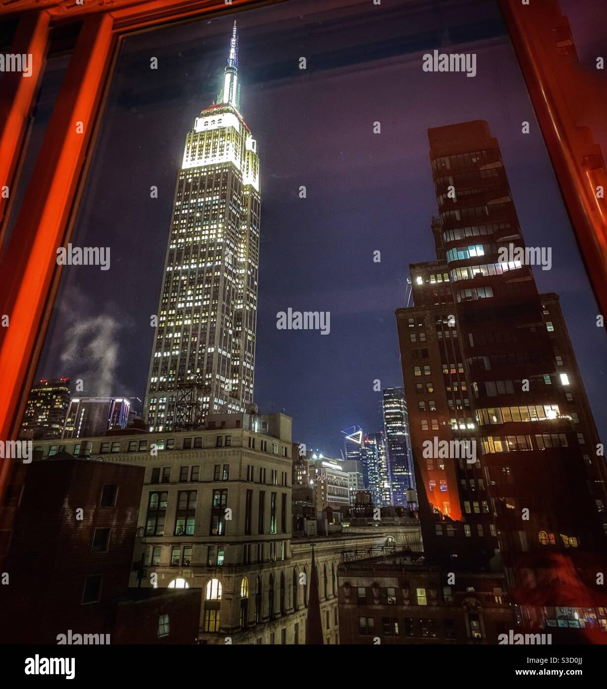 A Weat Facing Evening View Out An Apartment Window Of New York City Skyscrapers Punctuated By The Glamorous Landmark Empire State Building Lit Up With White Lights Hudson Yards In The Background