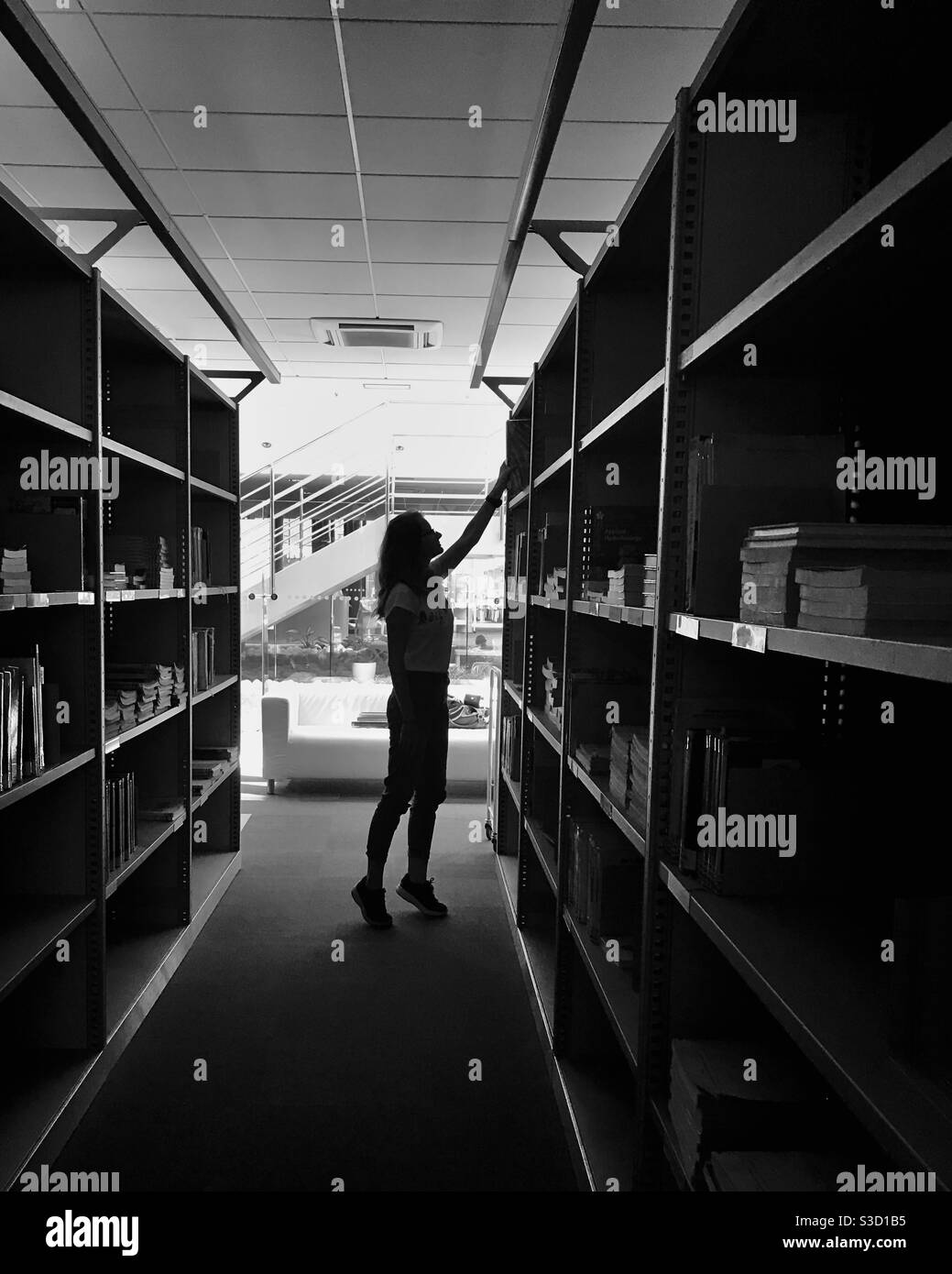 Girl in a library standing on tiptoes reaching for a book on the