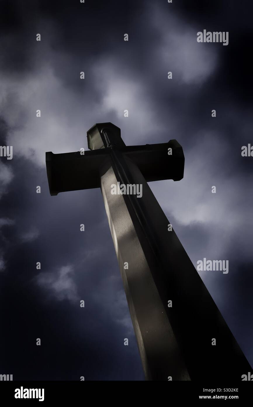 A dark and foreboding religious cross in a graveyard under a stormy sky ...