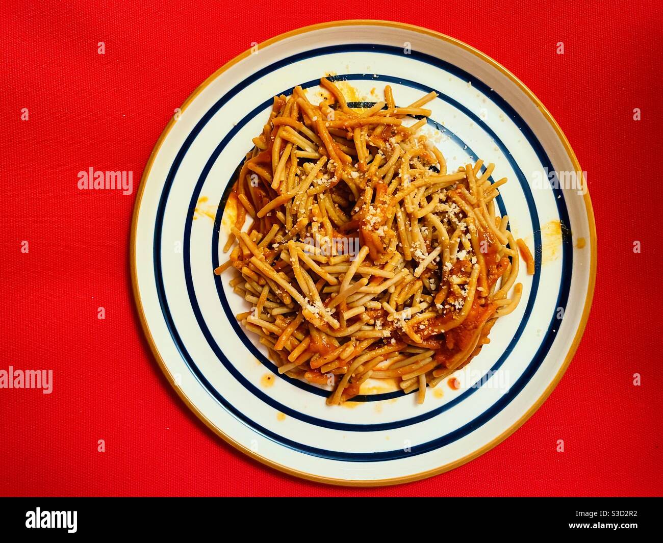 Pasta with marinara sauce on a white place with blue circular lines on a red tablecoth. Stock Photo