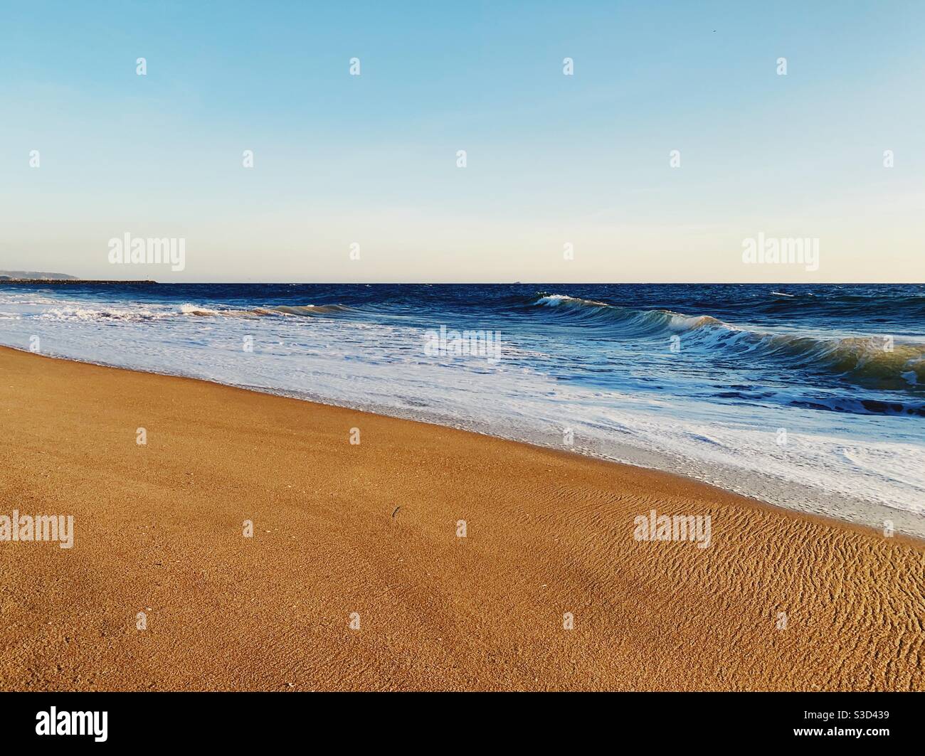 Seascape of sandy beach with ocean waves washing up on a sunny late afternoon. - Smartphone Captured Stock Image