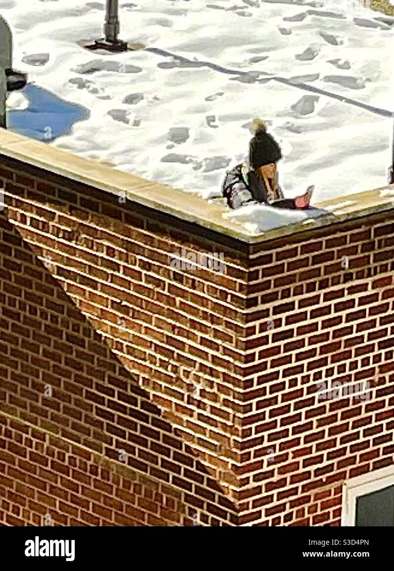 When you want privacy for your phone call, go up to the roof as this woman did on a sunny but cold winter day in Manhattan, New York, USA, bundled up in a down jacket & knit hat with a pom pom. - Smartphone Captured Stock Image