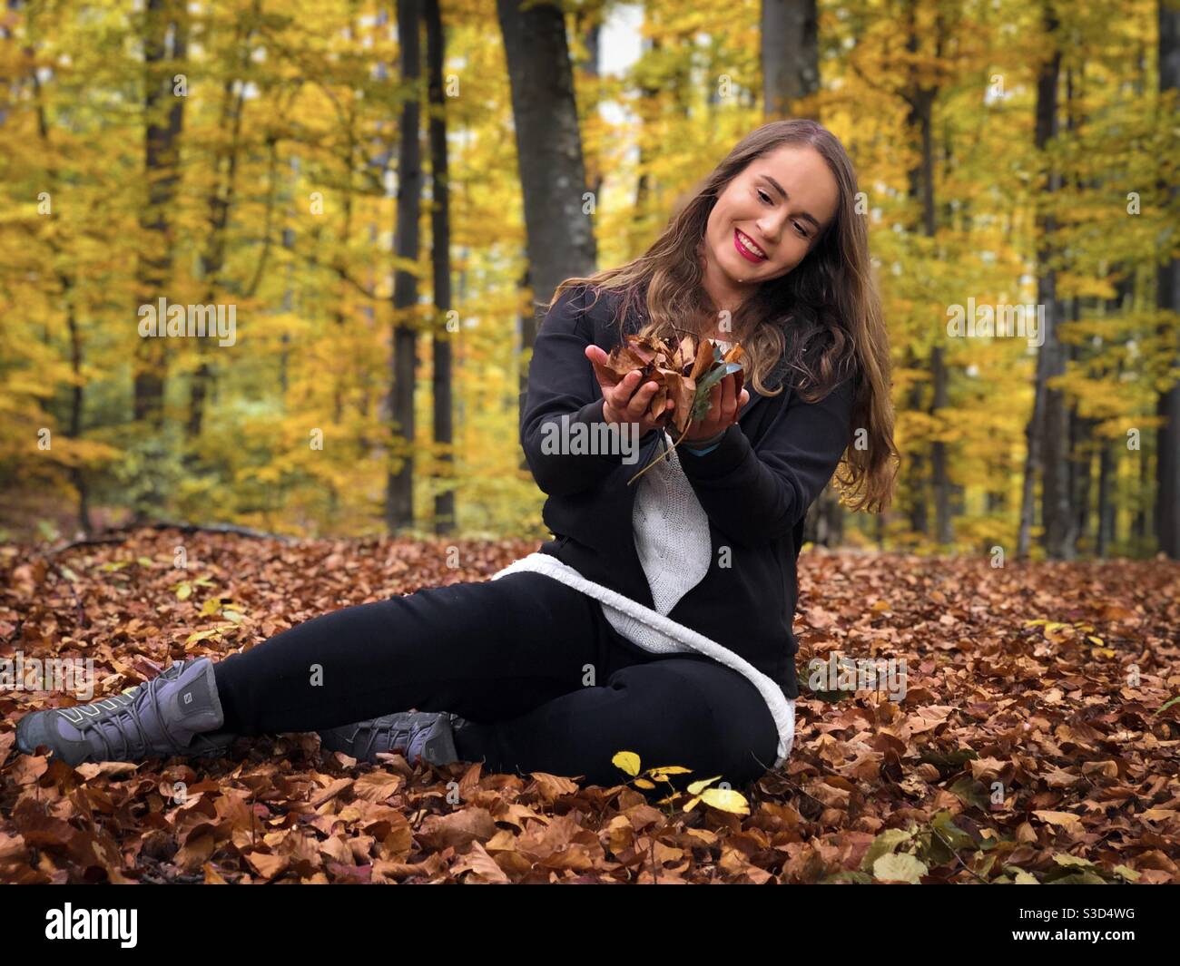 Young woman in the forest holding autumn leaves in her hands - Smartphone Captured Stock Image