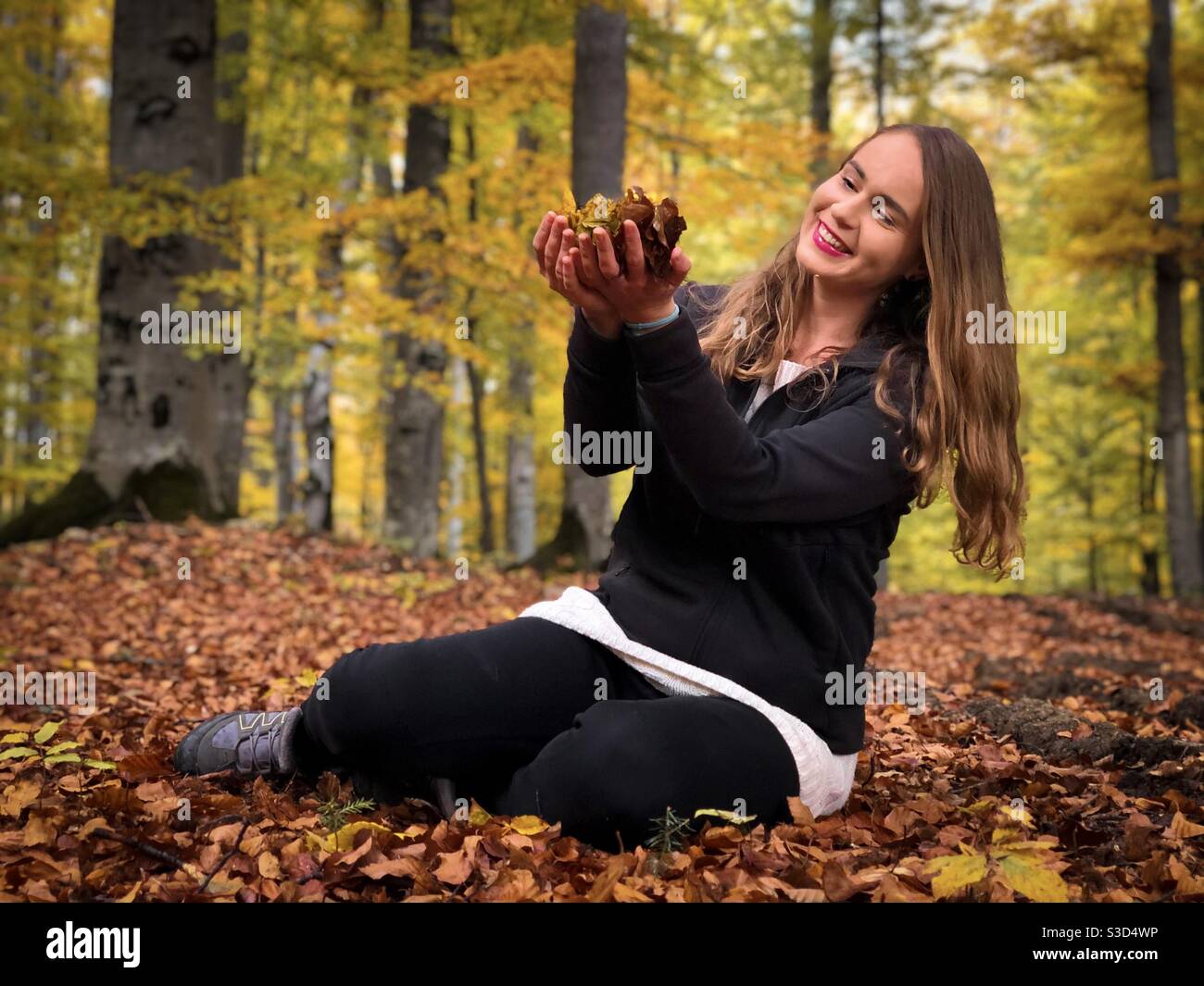 Young woman in the forest holding autumn leaves in her hands - Smartphone Captured Stock Image