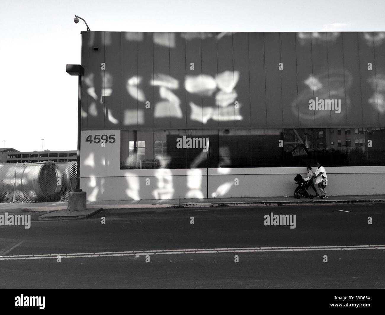 Odd reflections on the side of a building as a woman passes by pushing a stroller. - Smartphone Captured Stock Image