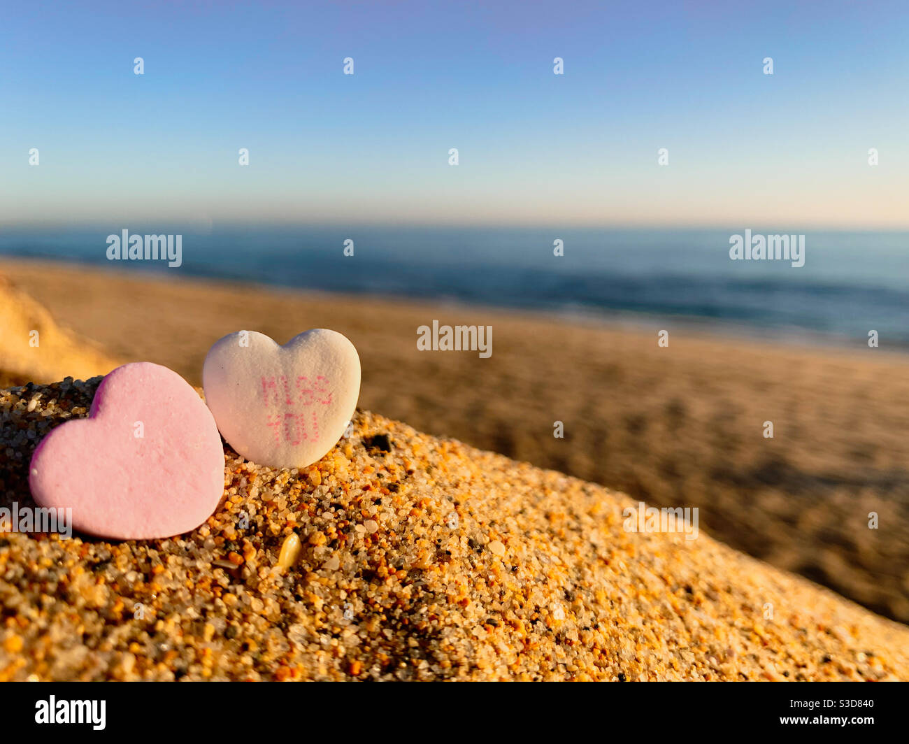 Two Valentine heart shaped candies on a sunny beach. One of the candies has the words miss you on it. - Smartphone Captured Stock Image