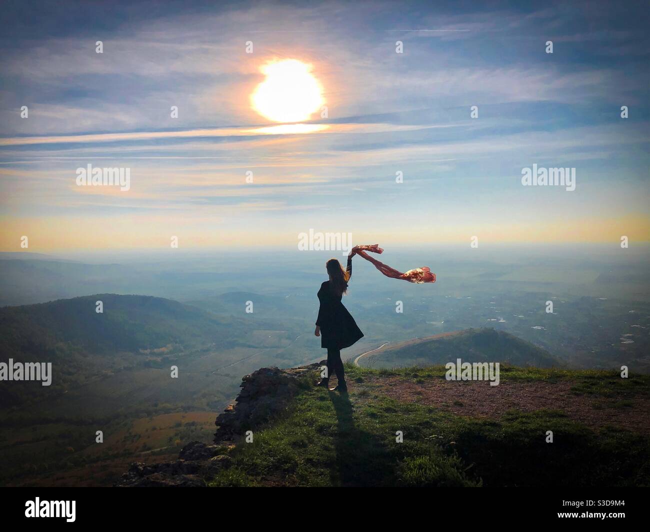 Woman standing on the edge of a cliff holding a scarf blowing in the wind - Smartphone Captured Stock Image