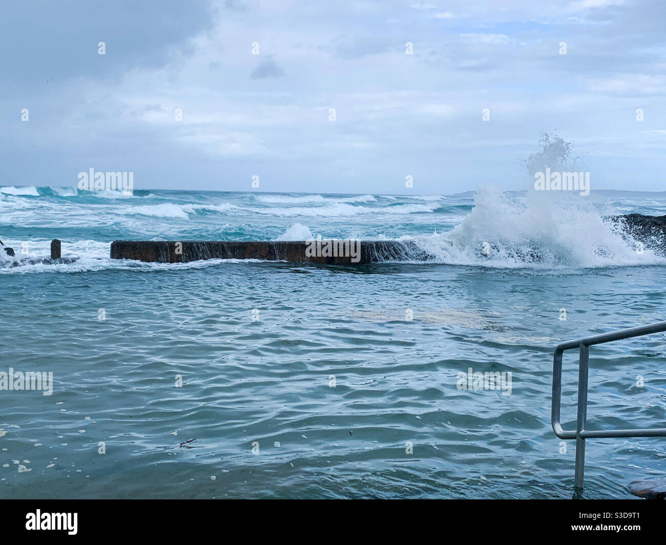 Waves crashing into the rock pool, Pacific Ocean beyond and metal handrail in foreground - Smartphone Captured Stock Image
