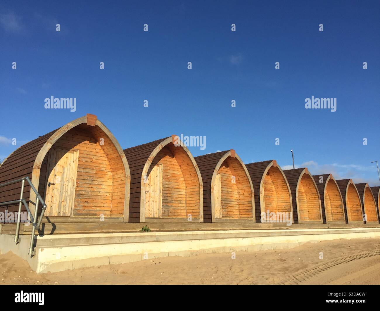 A row of modern wooden beach or shepherds huts under a blue sky at the beach - Smartphone Captured Stock Image