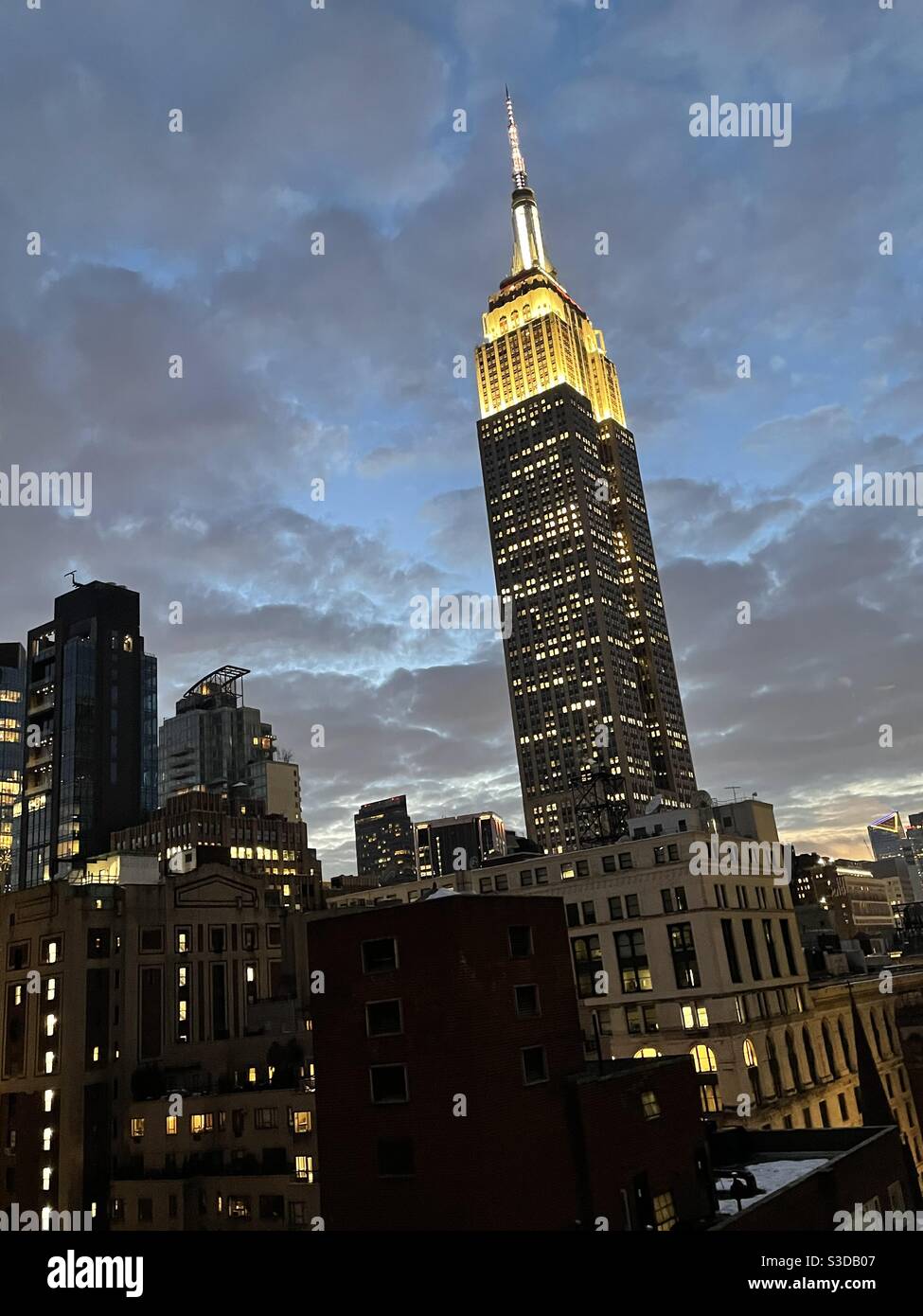Silhouette of the Empire State building with golden white lights against the twilight sky with puffy gray clouds before a storm, New York City, USA - Smartphone Captured Stock Image