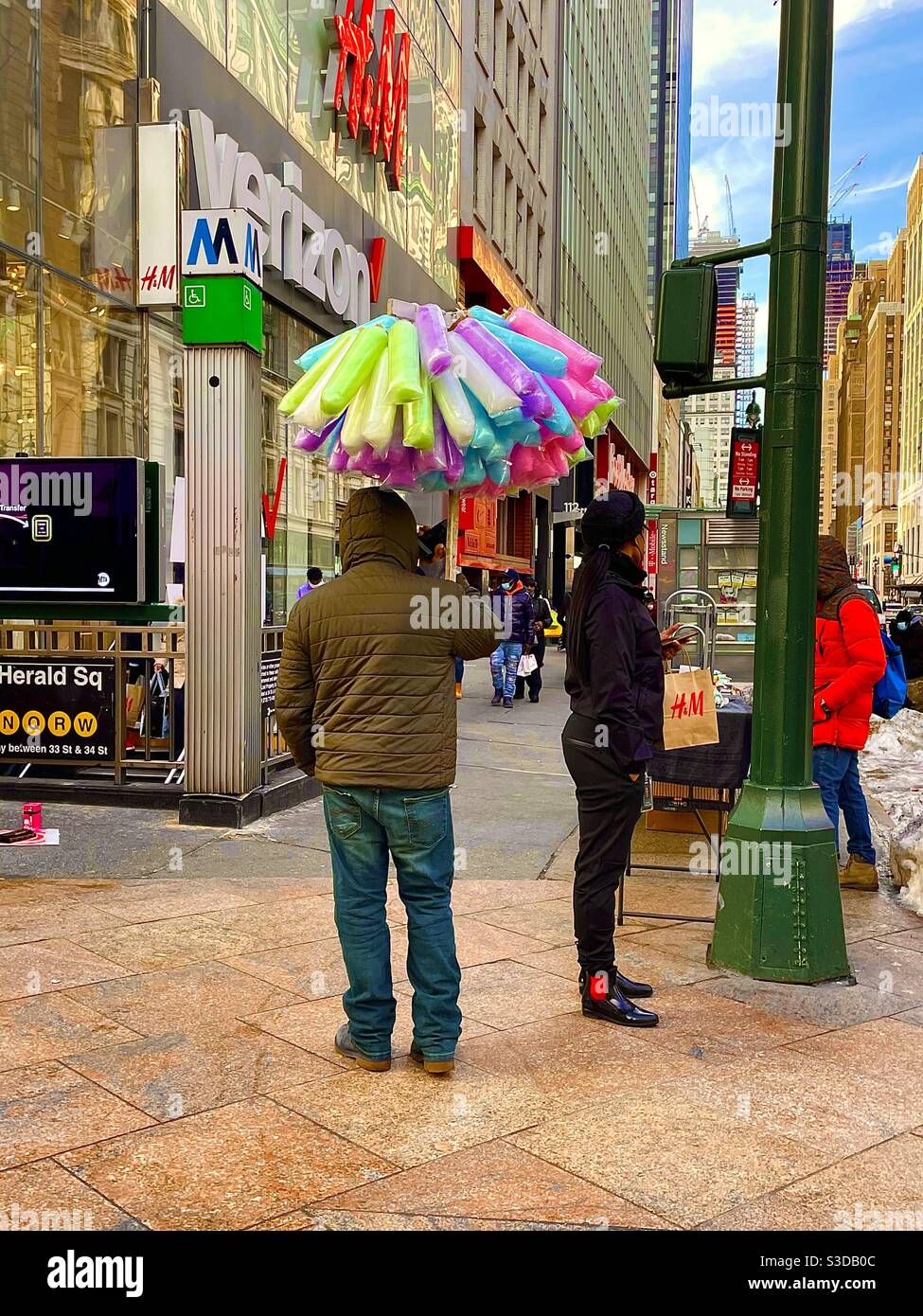 A man sells balloons on the sidewalk in Herald Square at the intersection of Avenue of the Americas and 34th St. across from Macy’s, by the Herald Square Subway station entrance, - Smartphone Captured Stock Image