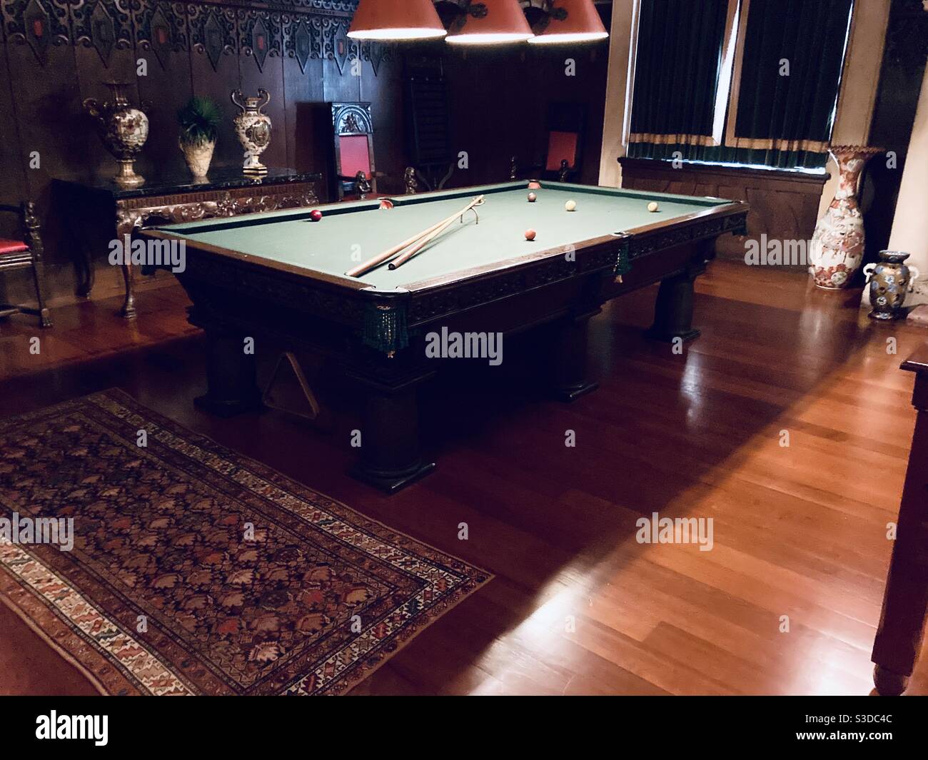 A classic picture of the billiard room a pool table in a dark wood room. Two pool cues on the table along with colored balls ready for a game Stock Photo