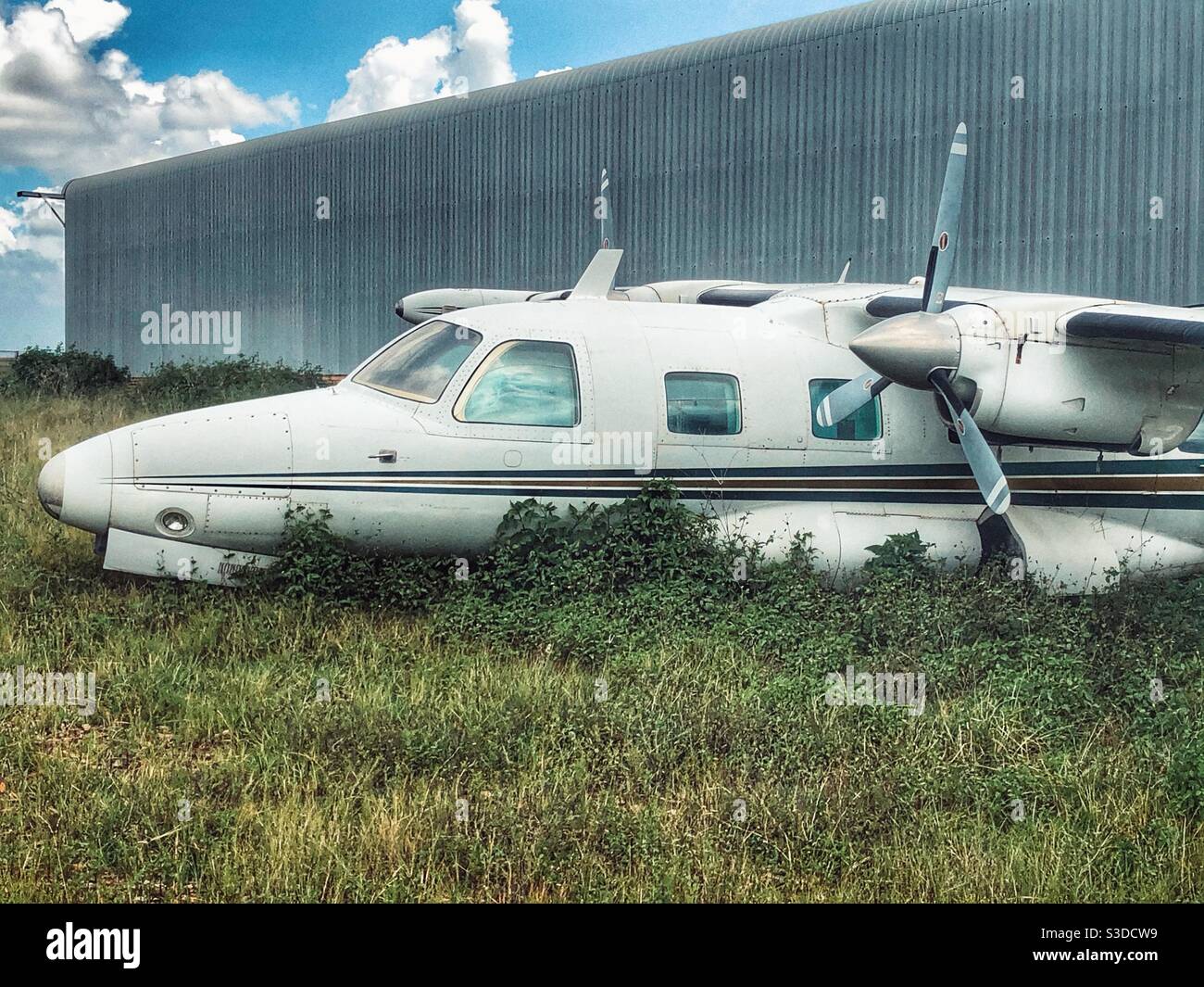 Abandoned aeroplane parked in overgrown grass next to hangar - Smartphone Captured Stock Image