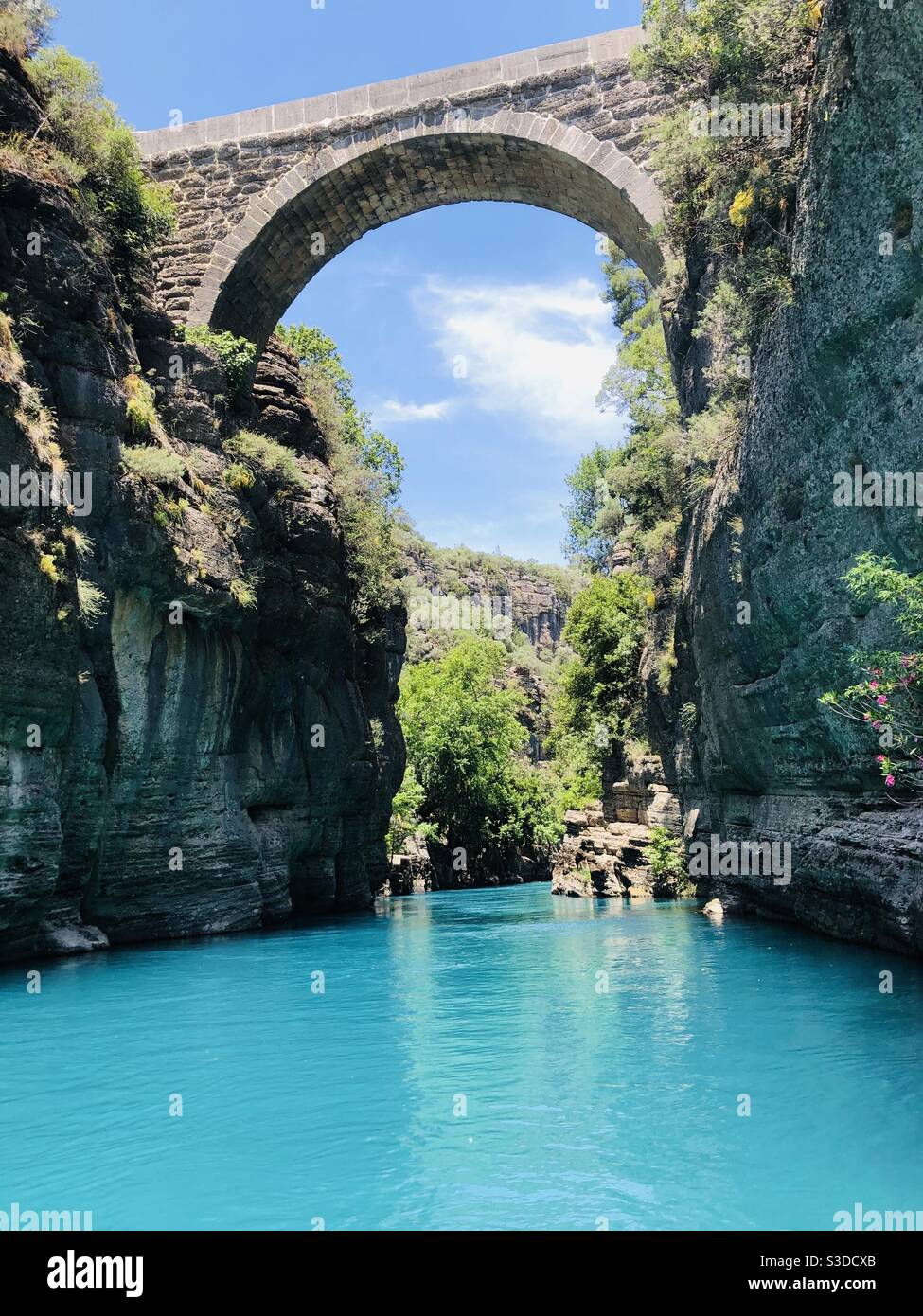 An ancient bridge built just above this amazingly turquoise flowing river between the mountains Stock Photo