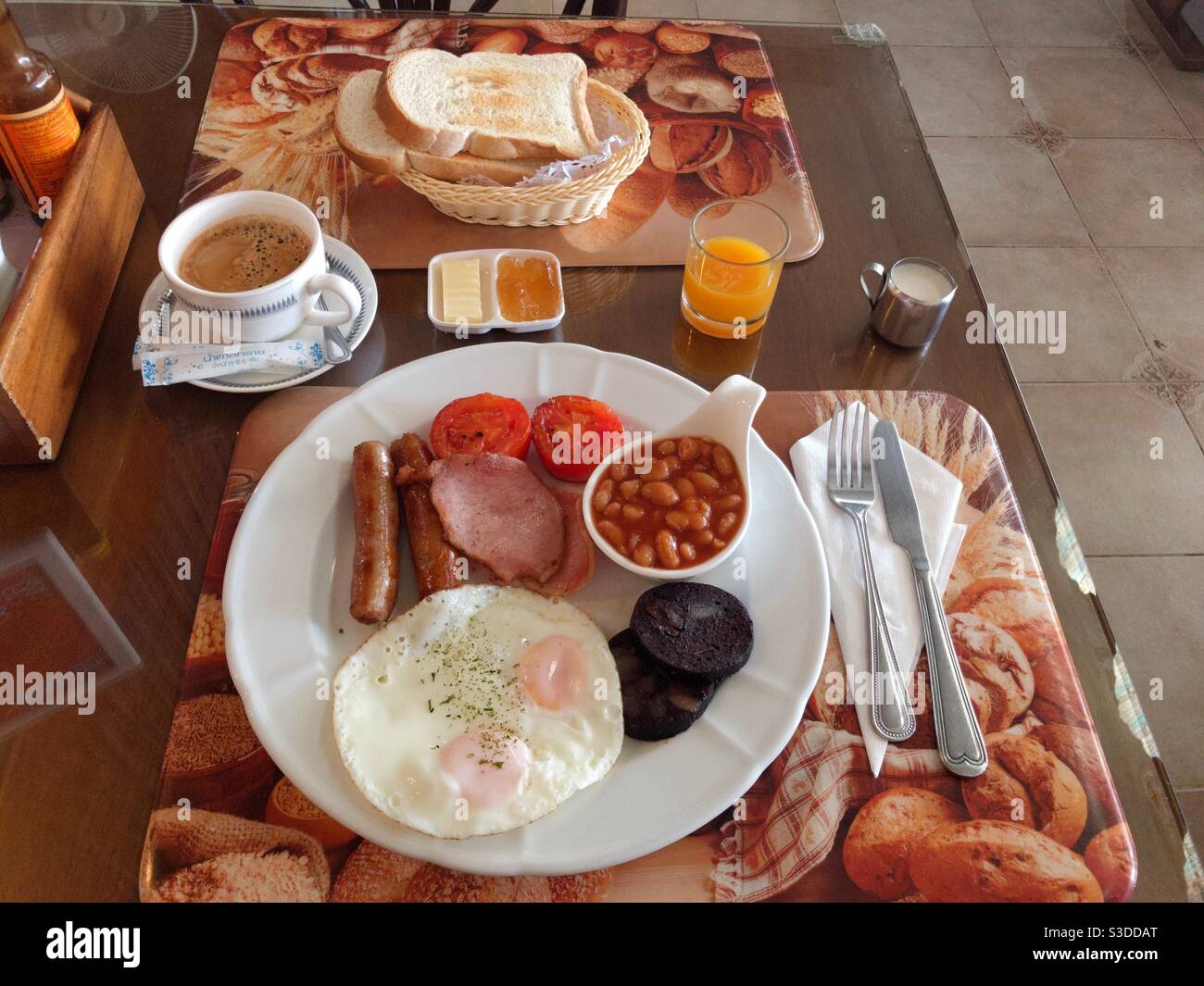 Full English breakfast of bacon, eggs, sausage, grilled tomatoes, black pudding and baked beans with coffee, orange squash, toast and marmalade - Smartphone Captured Stock Image