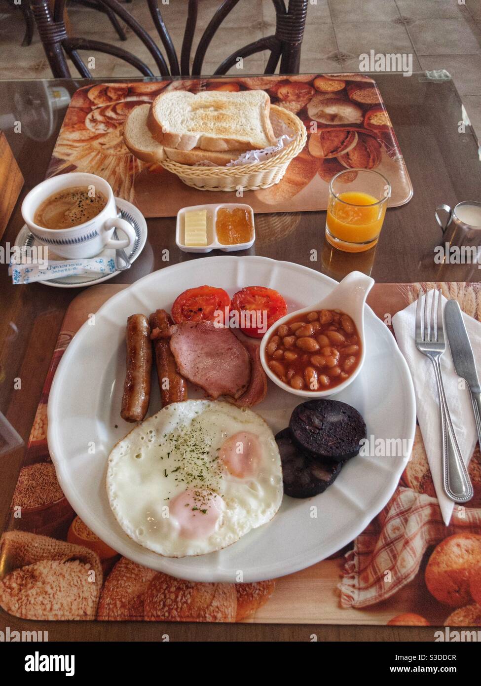 Full English breakfast of bacon, eggs, sausage, grilled tomatoes, black pudding and baked beans with coffee, orange squash, toast and marmalade - Smartphone Captured Stock Image