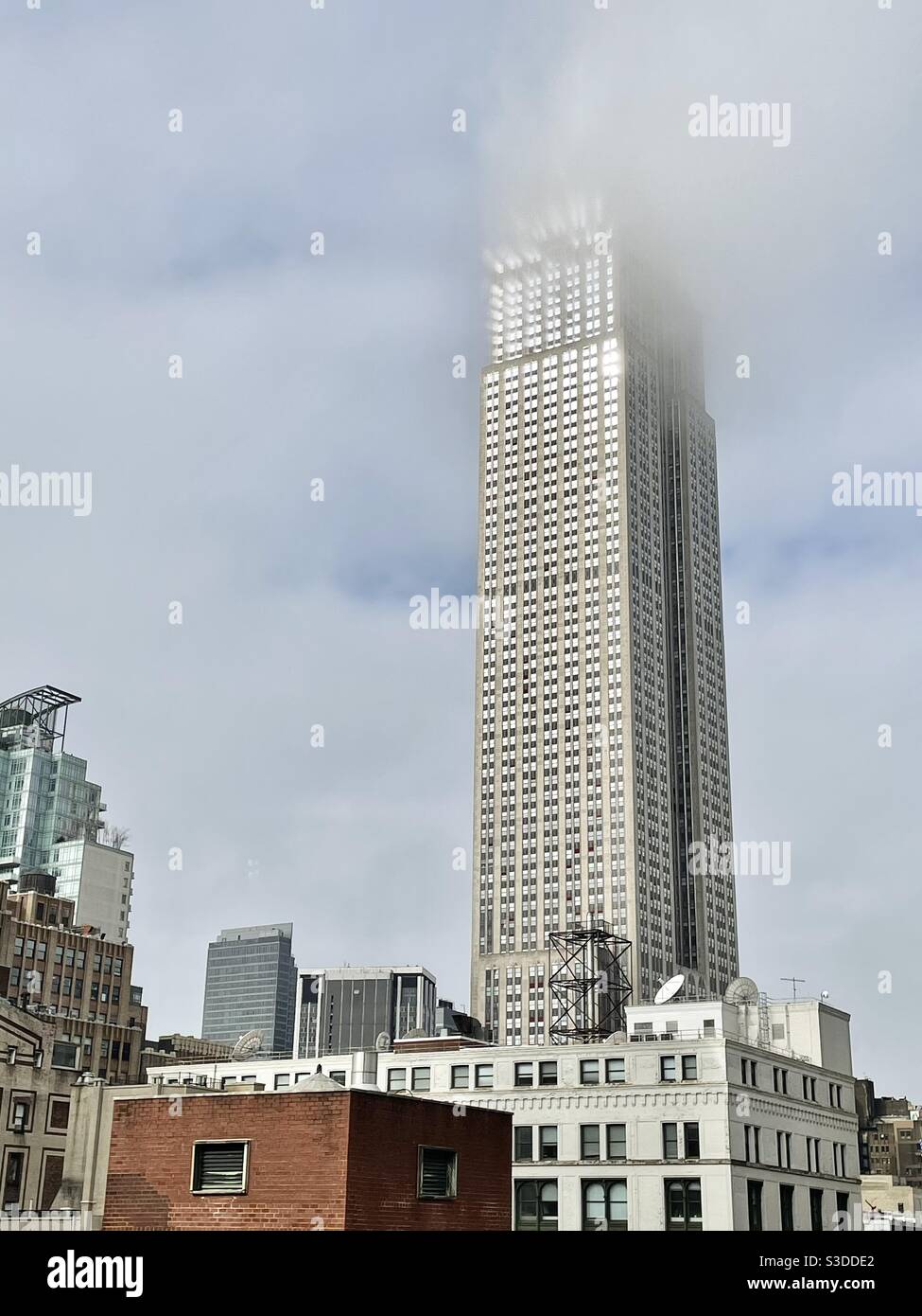 Sun and fog play on the upper levels of the Empire State building and glisten off the windows as a low cloud dances around the top of this iconic sky scraper in Manhattan USA - Smartphone Captured Stock Image