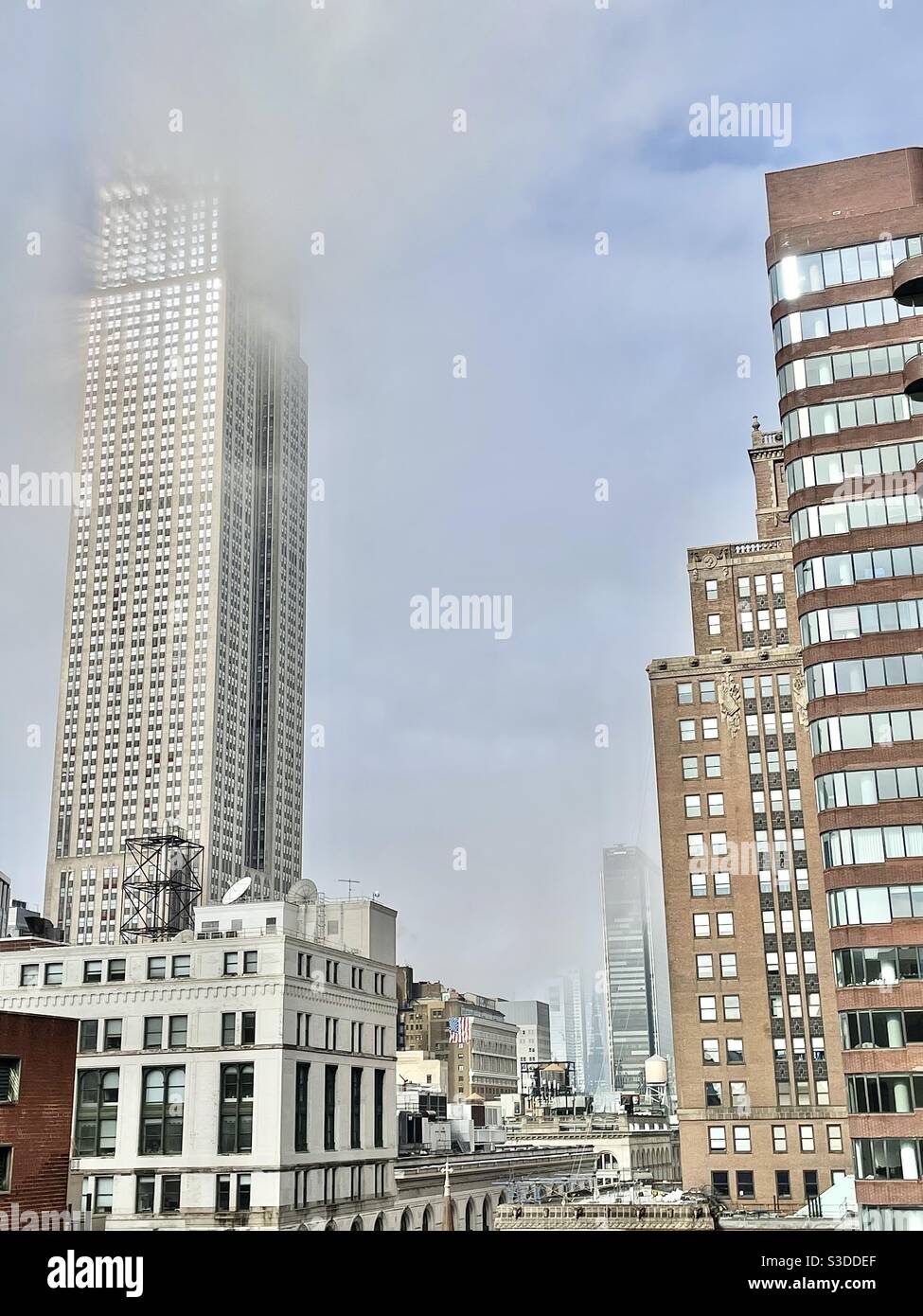 The Empire State building reaches for the sky and touches the clouds as sunlight reflects on skyscraper windows in midtown Manhattan with a view of Hudson yards in the background, New York City, USA - Smartphone Captured Stock Image