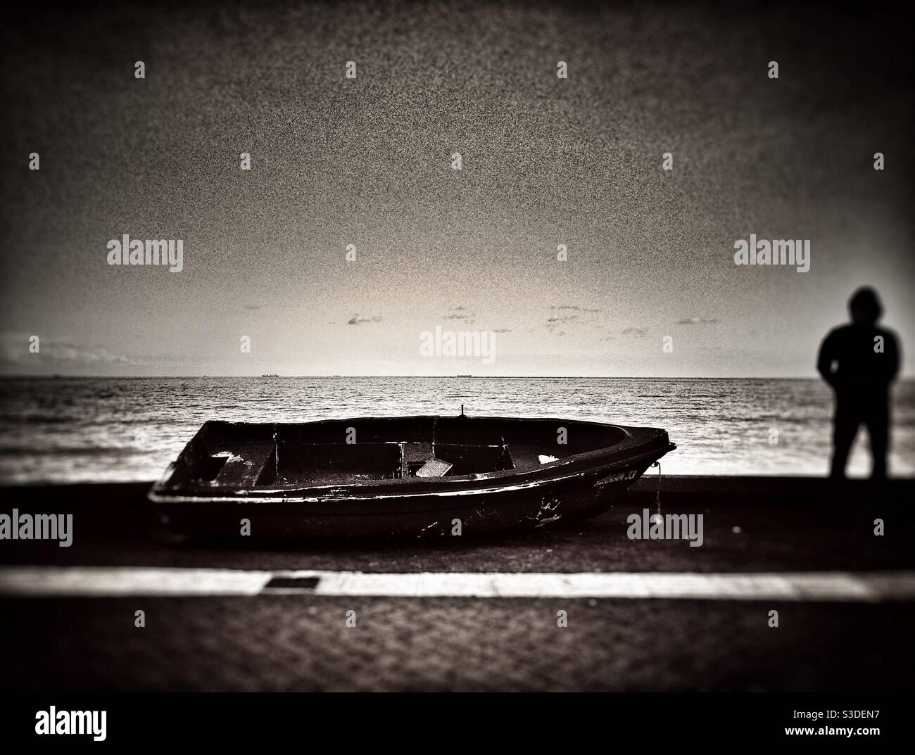 Fishing boat left by the sea and silhouette of a man standing next to it - Smartphone Captured Stock Image