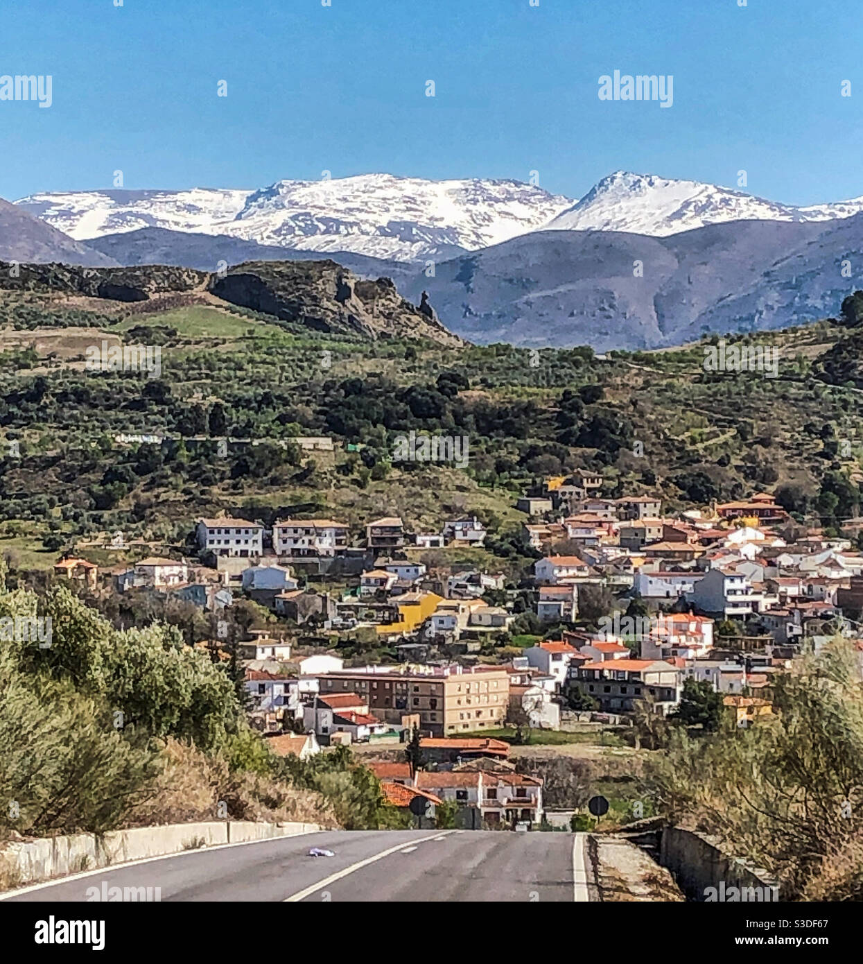 Follow the road down to Beas de Granada with the snow capped peaks of the Sierra Nevadas Stock Photo