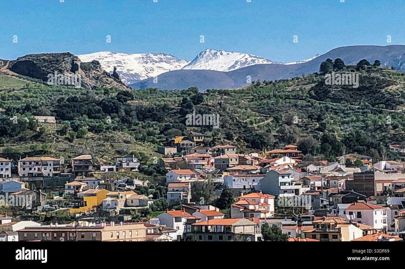 Beas de Granada nestled in the valley below the snow topped peaks of Sierra Nevadas, Spain Stock Photo