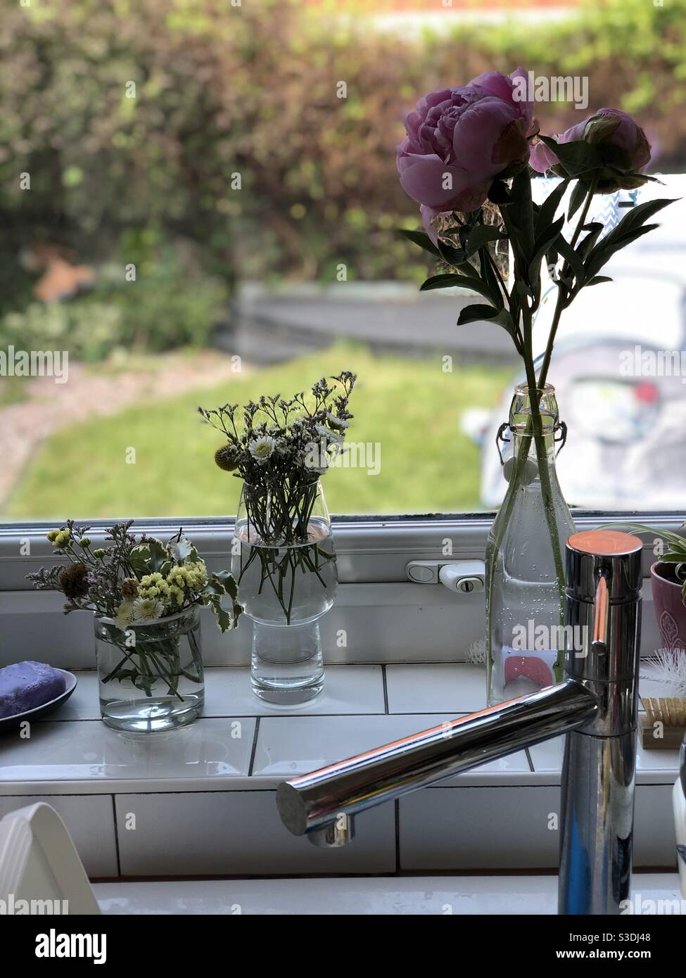 Dried flowers and peonies in bottles and glasses on a kitchen windowsill Stock Photo
