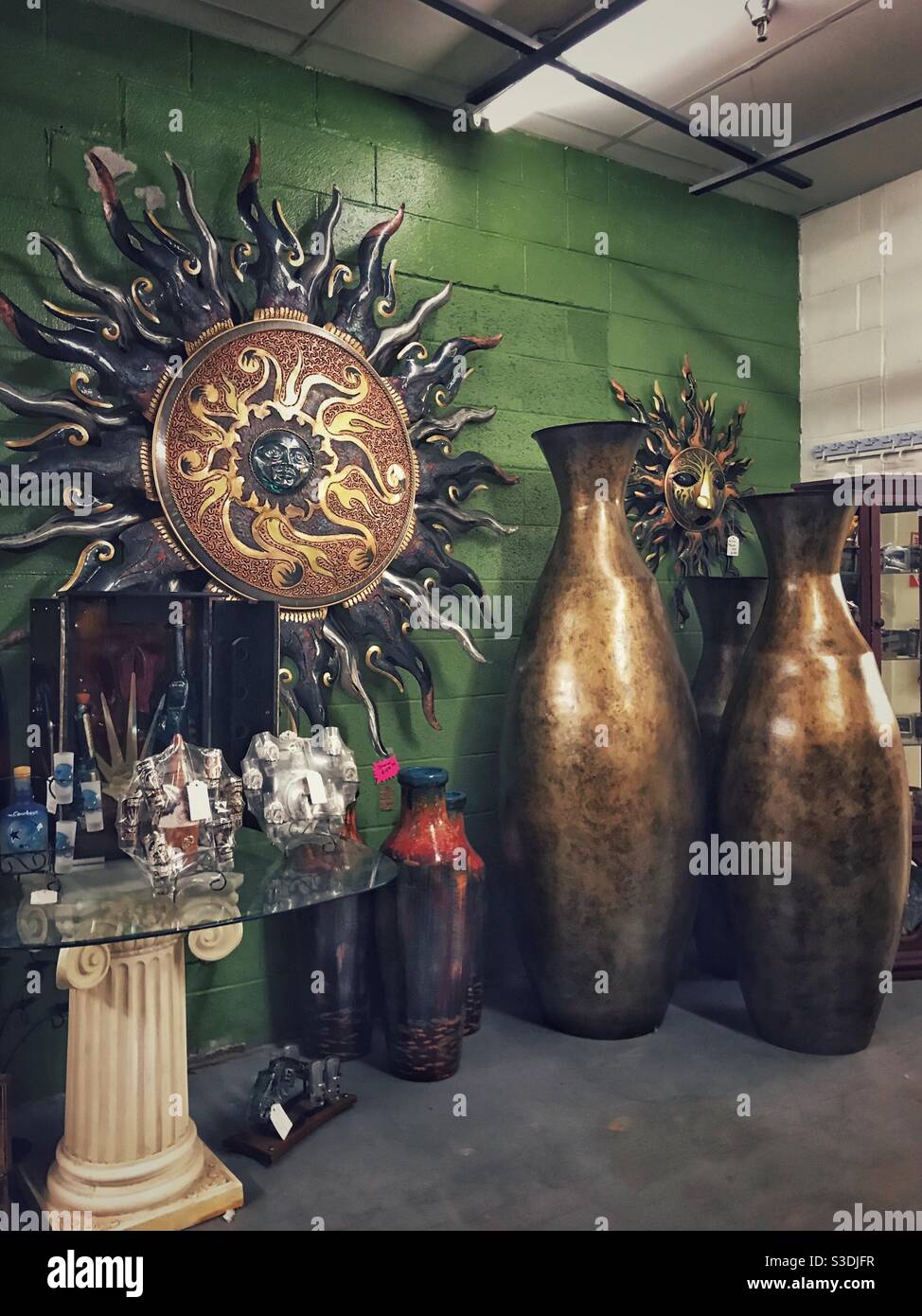 Ethnic sunburst wall art piece on display beside large bronze urns at antique mall - Smartphone Captured Stock Image