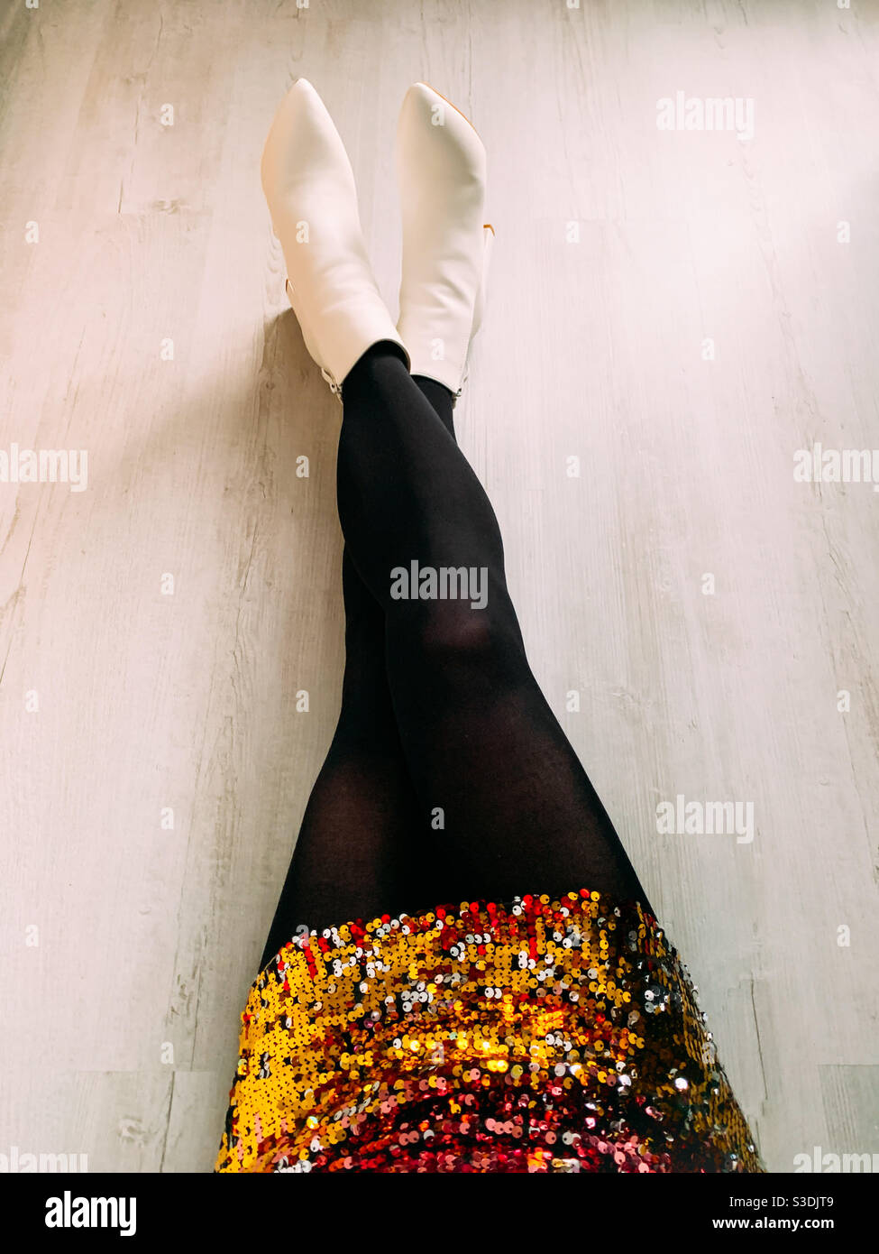 Woman sat on the floor wearing a sequin dress and white ankle boots Stock Photo