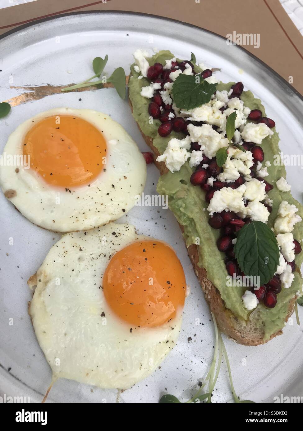 Creamy avocado on sourdough bread topped with pomegranate seeds and crumbled feta cheese and two medium fried eggs - Smartphone Captured Stock Image