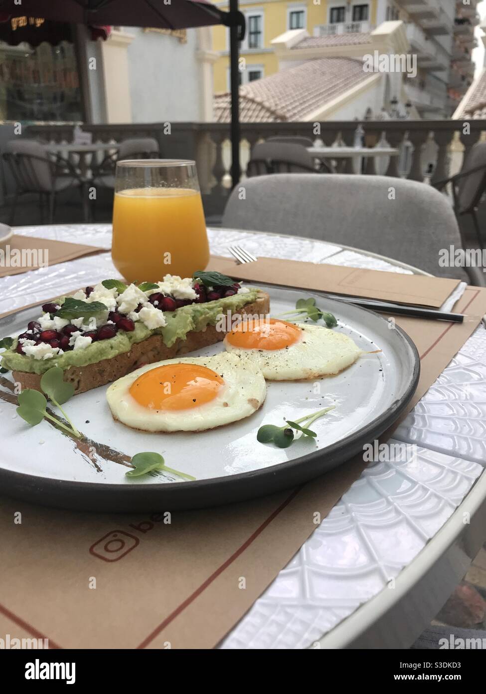Creamy avocado on sourdough bread topped with pomegranate seeds and crumbled feta cheese and two medium fried eggs served with fresh orange juice - Smartphone Captured Stock Image