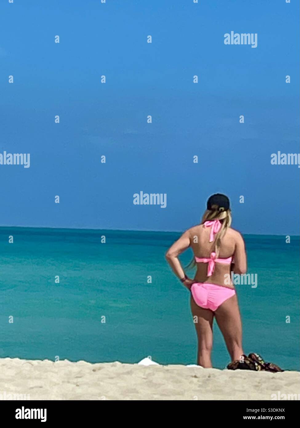 A bikini clad blonde woman On Miami Beach Gazes at the turquoise ocean & clear blue sky On a perfect beach day in February, Florida, USA - Smartphone Captured Stock Image