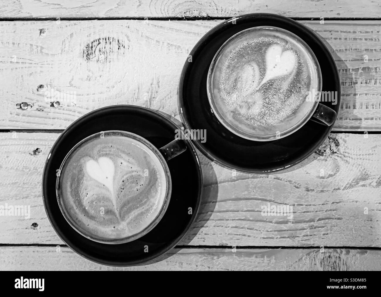 Two cups of coffee with heart shaped latte art on wooden table top - Smartphone Captured Stock Image