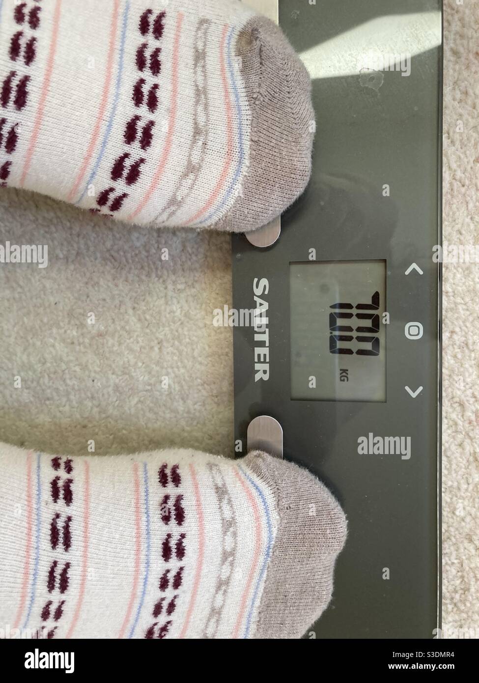 A woman wearing patterned socks weighing herself on a pair of electric scales Stock Photo