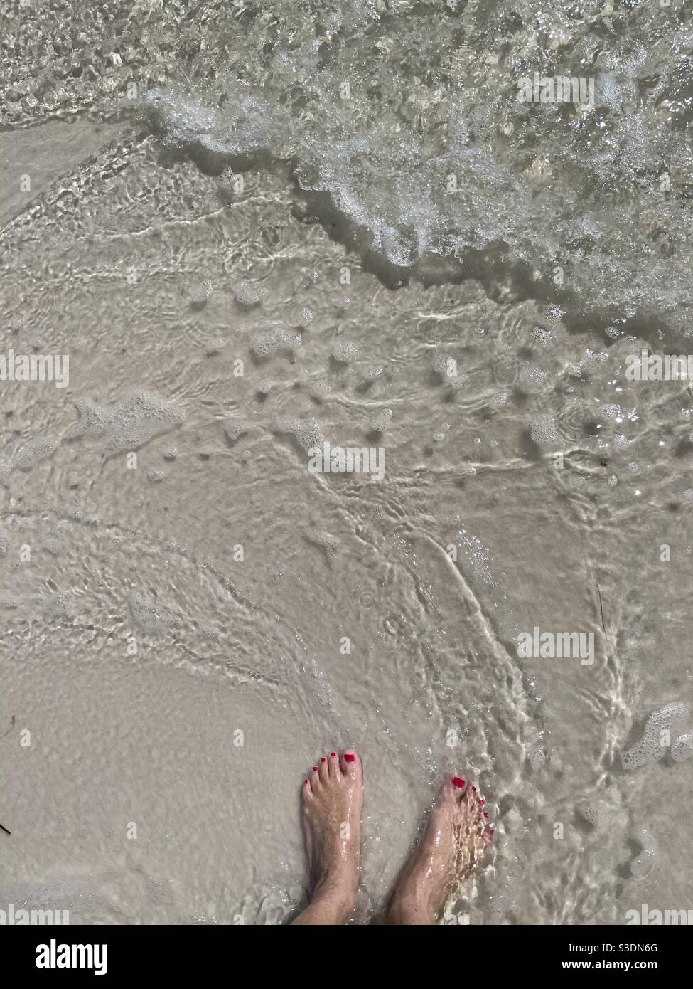 Feet standing in the sand with ocean waves - Smartphone Captured Stock Image