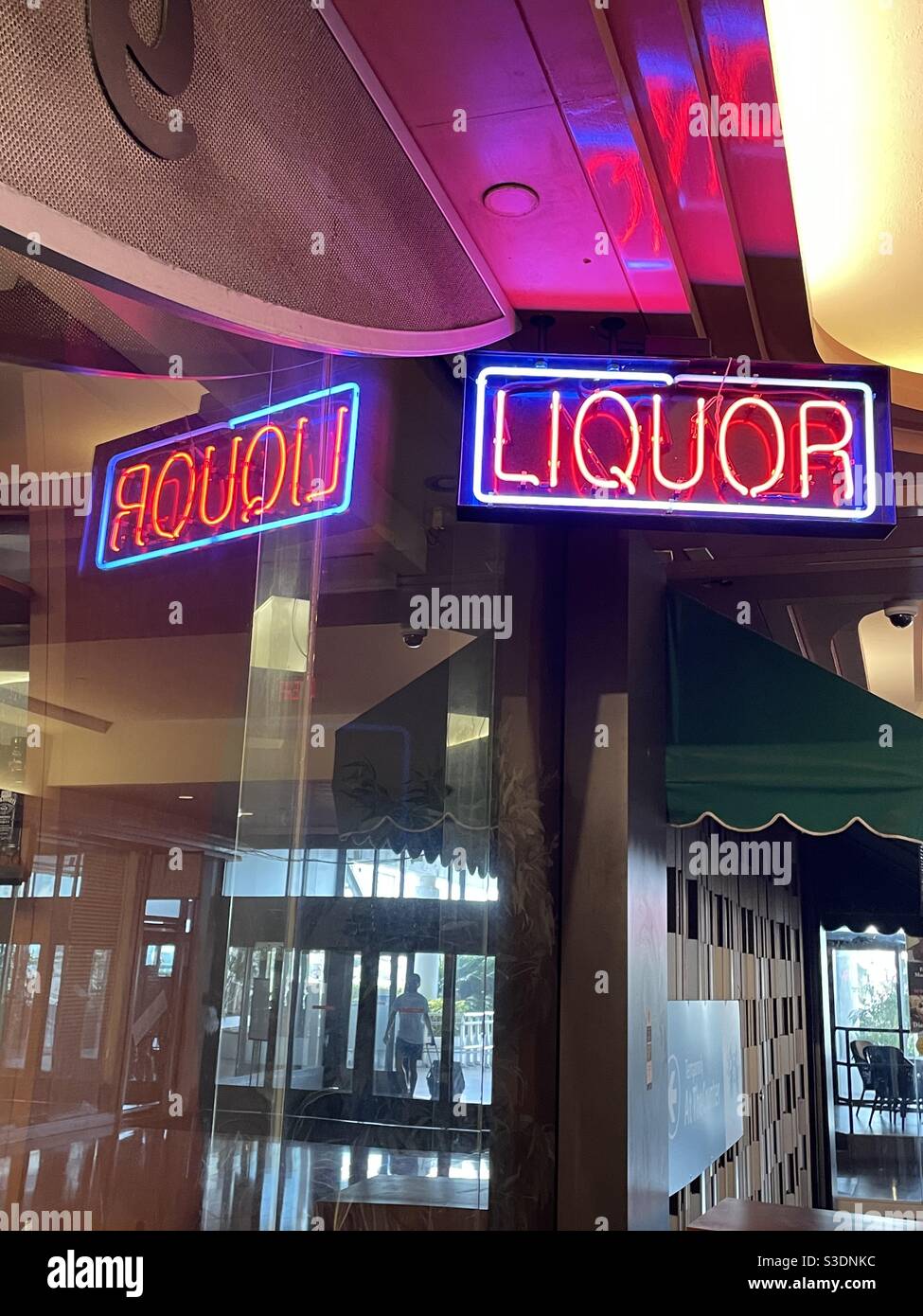 A red & white neon sign saying “liquor” is reflected backwards in the glass windows of a shop in the retail plaza of the Doubletree hotel in downtown Miami, Florida, USA. - Smartphone Captured Stock Image