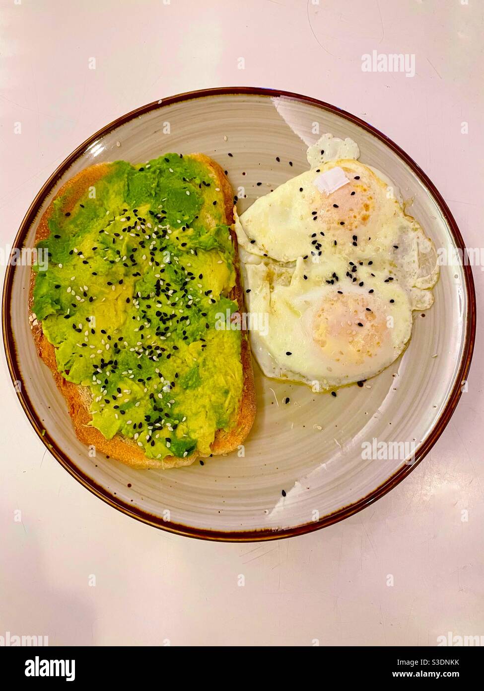 A popular & delicious healthy meal is avocado toast with eggs cooked over-easy sprinkled with black sesame seeds Served on a brown edged plate - Smartphone Captured Stock Image