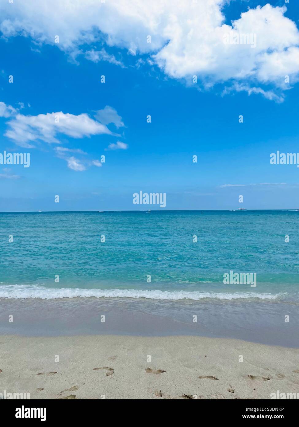 Miami Beach, Florida, USA boasts dazzling colors of bright blue skies with fluffy white clouds, an ocean that changes from deep blue to turquoise as the white foamy surf breaks on a sandy beach Stock Photo
