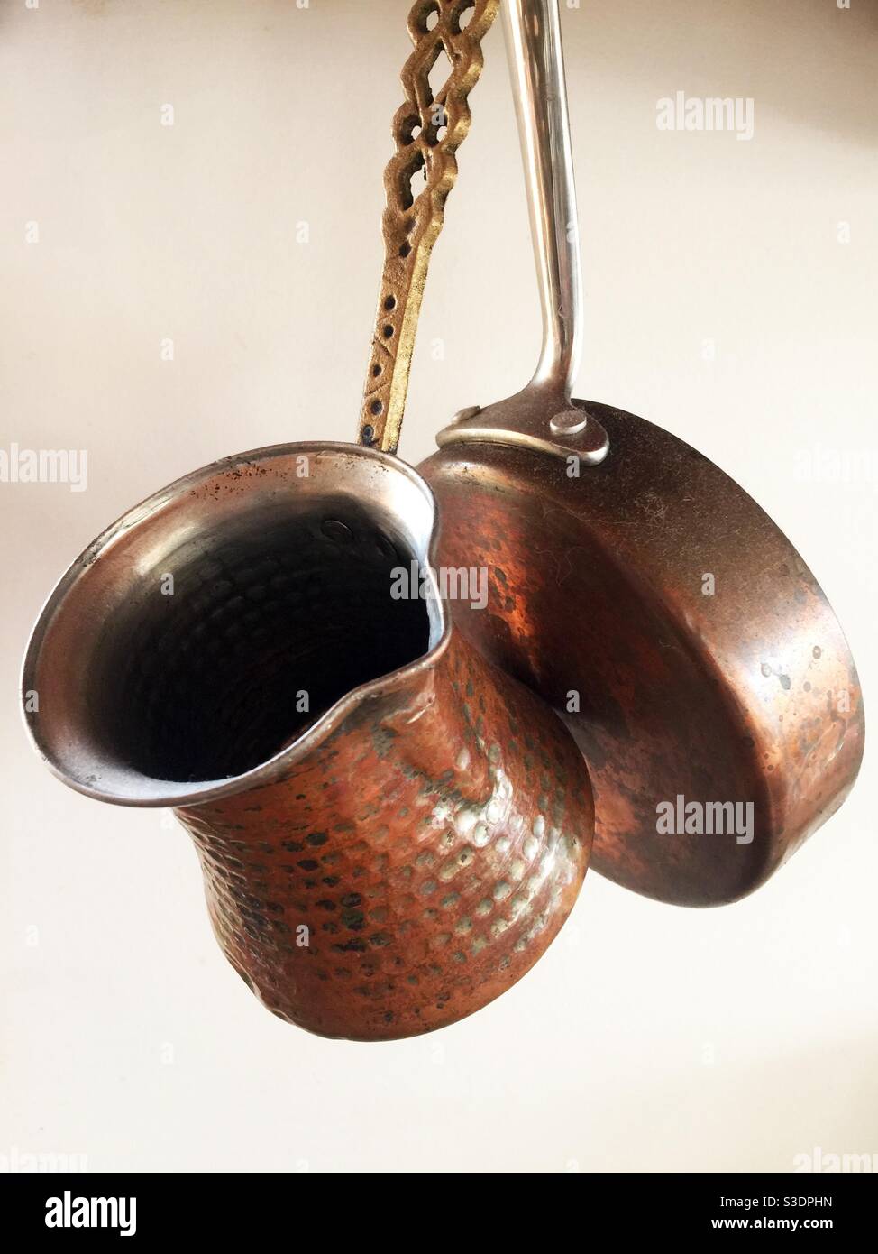 A copper pot and pan, everyday items in a kitchen, hang from a hook in the ceiling, seen against a light coloured wall, Canada. Storage as well as decor. - Smartphone Captured Stock Image