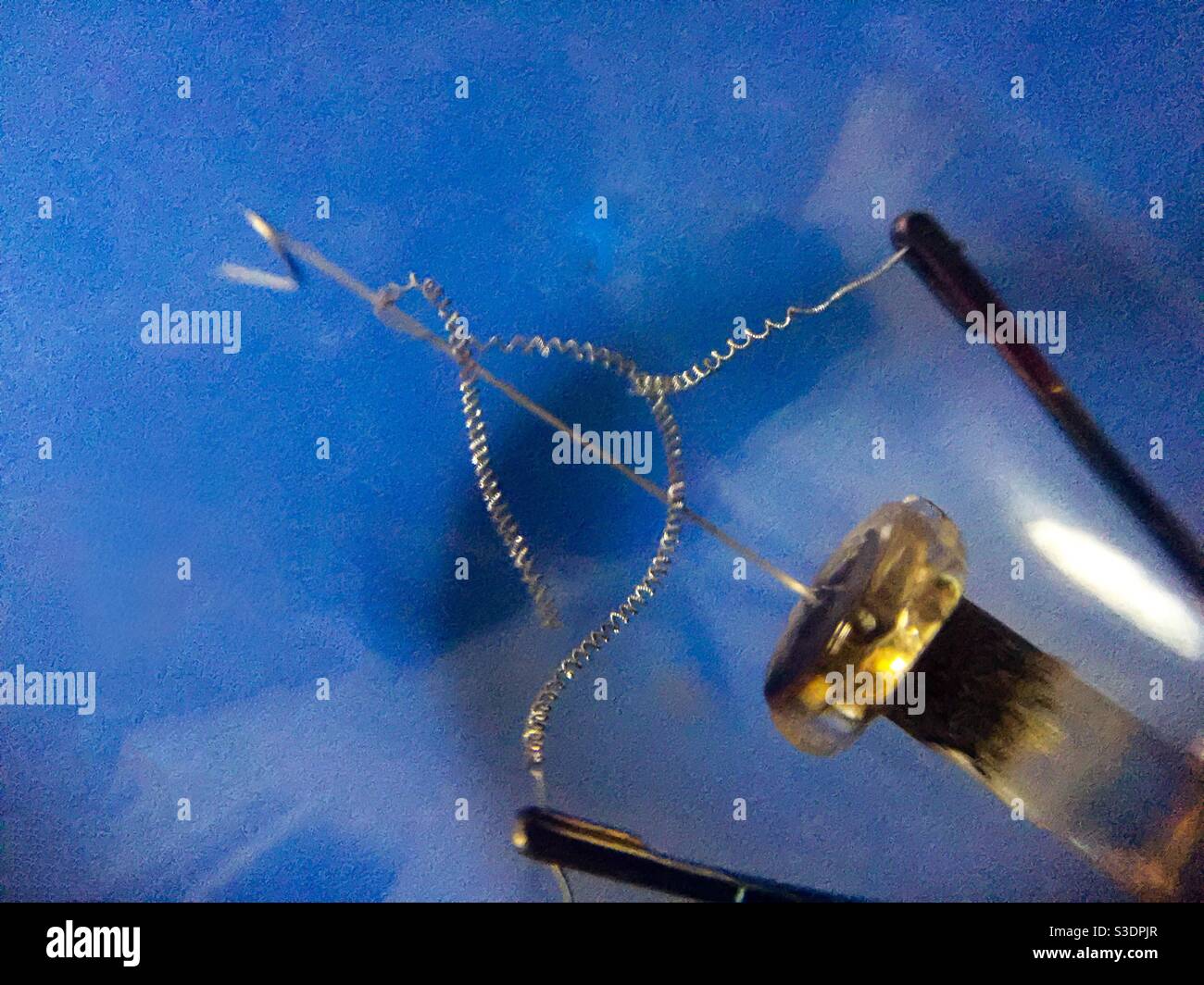 Broken filament of a fused bulb against a blue backdrop - Smartphone Captured Stock Image