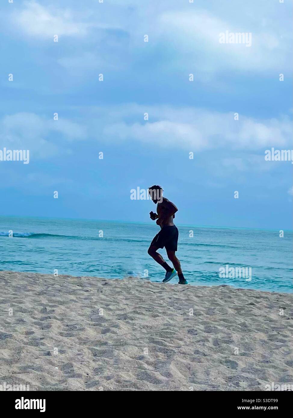 A man and swim trunks runs On the sand at the oceans edge in south Miami Beach, Florida, USA - Smartphone Captured Stock Image