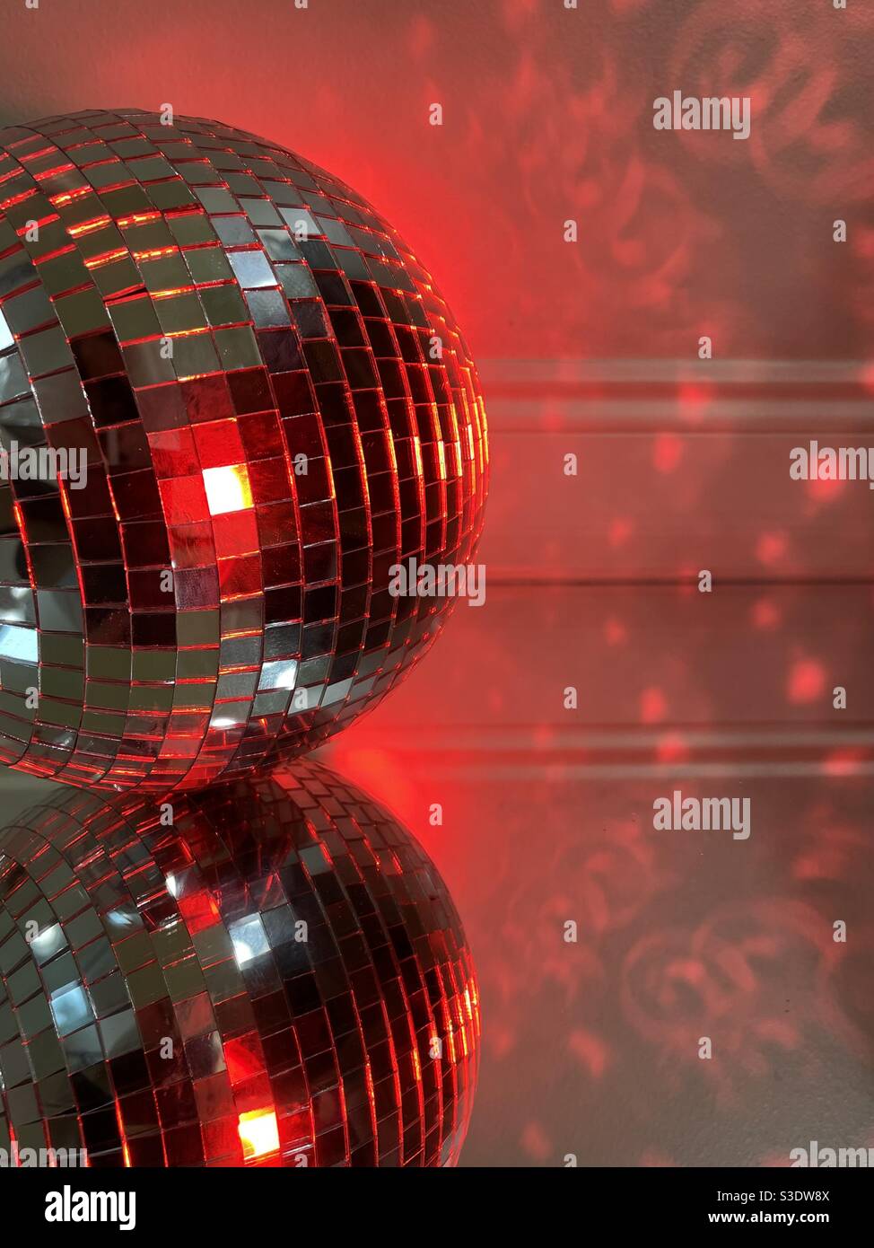 Disco ball with red lighting on mirrored surface with reflections Stock Photo