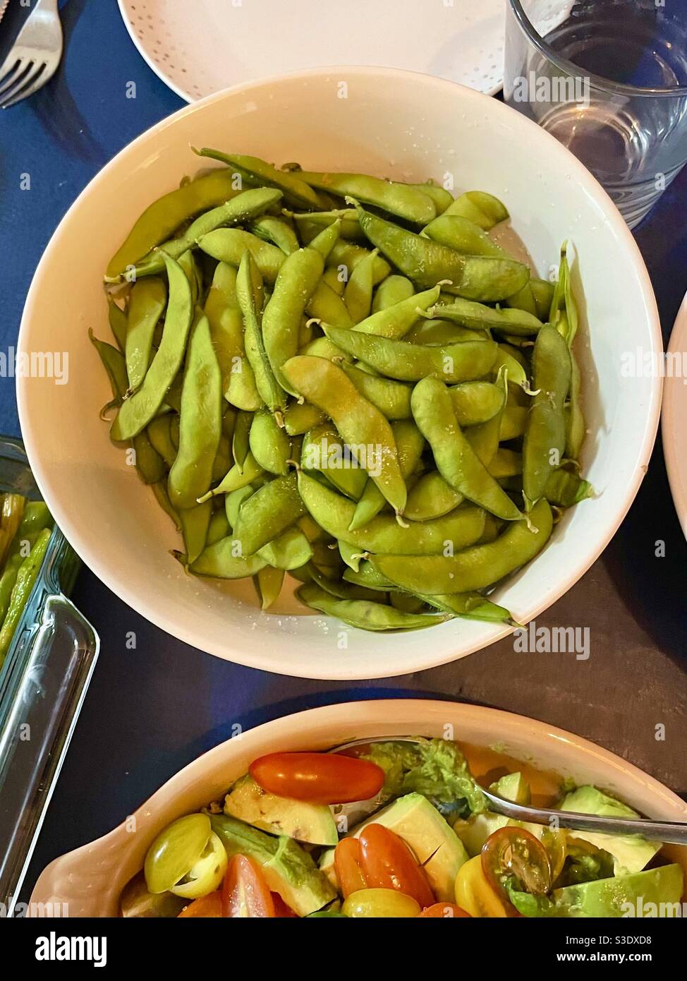 A white platter of edamame - soybeans - At a family meal beside a plate of mixed vegetables - Smartphone Captured Stock Image