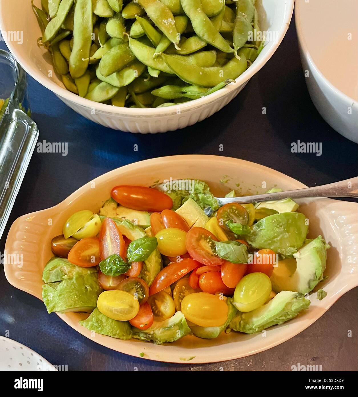 Two healthy side dishes served at a family meal - Tomatoes with brussels sprouts and a bowl of edamame or soy beans - Smartphone Captured Stock Image