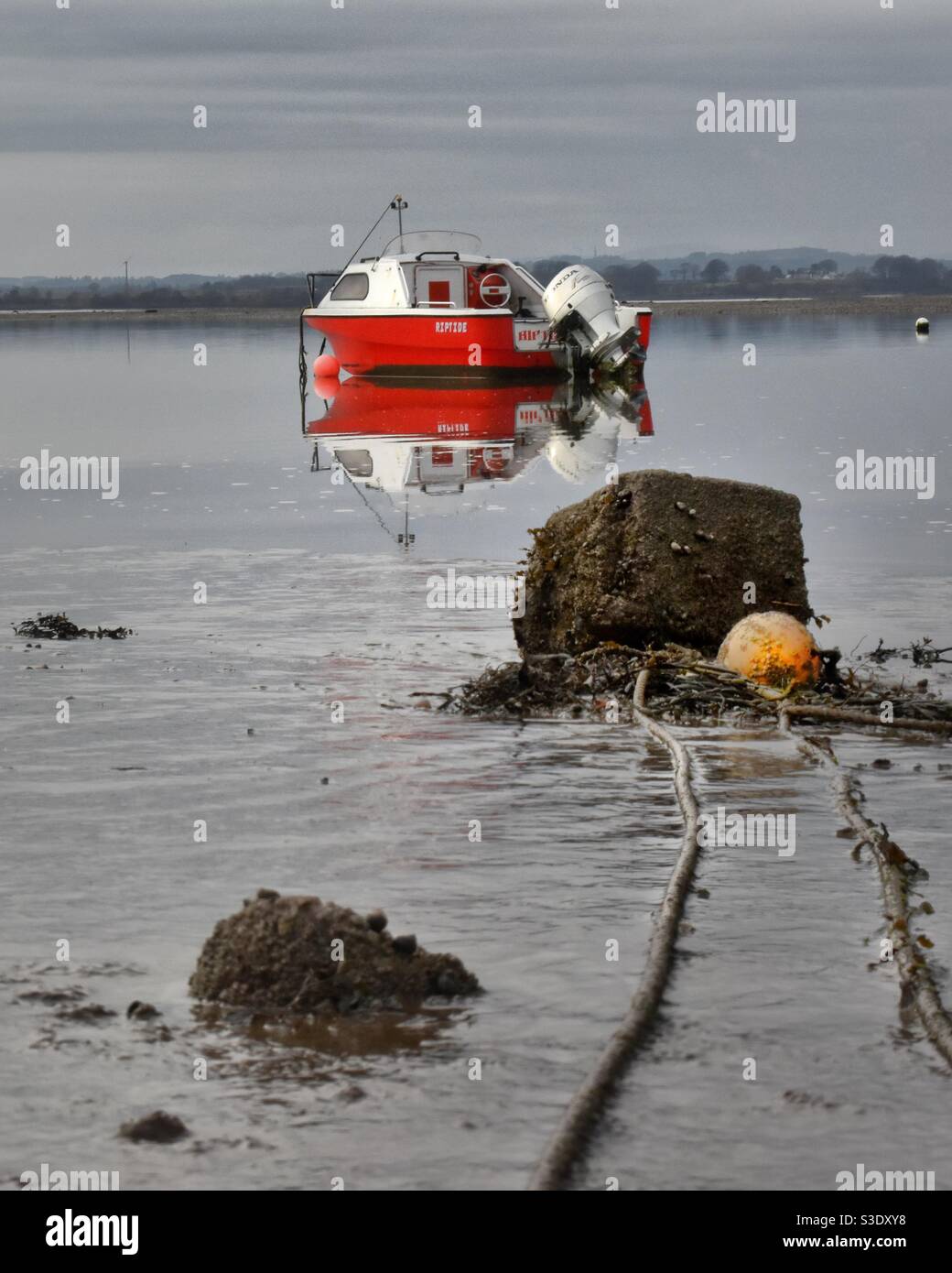 Red boat sits in calm waters on a dull day Stock Photo