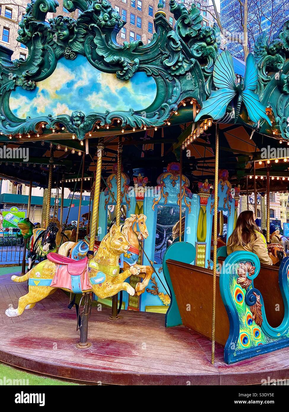 A dark-haired woman rides on the brightly-colored ornate carousel at Bryant Park, Manhattan, New York, USA - Smartphone Captured Stock Image