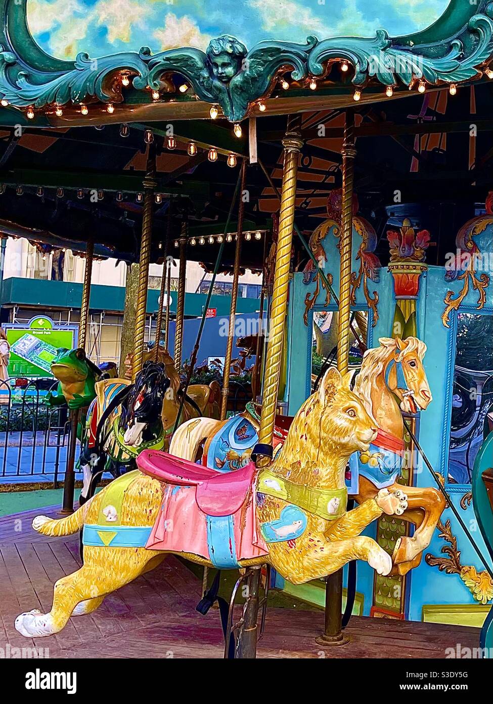 A beautiful golden carousel cat and horse followed by a green frog on the ornate colorful merry-go-round At Bryant Park, Manhattan, New York City, USA - Smartphone Captured Stock Image